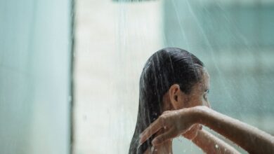 Persona bajo la ducha, con agua caliente y jabón, y una cantidad excesiva de agua derramada en el suelo.
