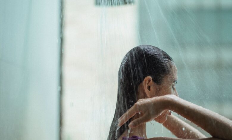 Persona bajo la ducha, con agua caliente y jabón, y una cantidad excesiva de agua derramada en el suelo.