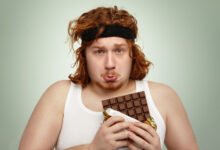 Joven deportista oliendo una barra de chocolate antes de hacer extensiones de piernas