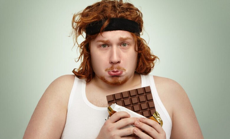 Joven deportista oliendo una barra de chocolate antes de hacer extensiones de piernas