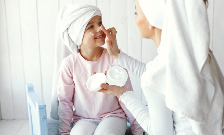 Niña aplicando varios productos de cuidado facial mientras su madre observa